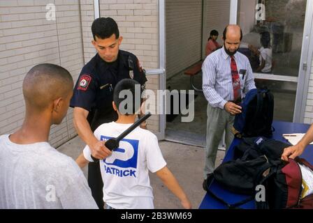 Austin Texas USA, um 1997: Ein Schulpolizist verwendet einen Metalldetektor, während ein Lehrer Rucksäcke inspiziert, wenn die Schüler zu Beginn des Schultages ihre Mittelschule betreten. ©Bob Daemmrich Stockfoto