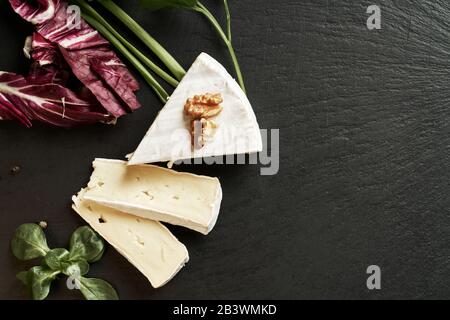 Köstlicher brie-käse auf schwarzem Hintergrund. Brie Käsesorte. Camembert. Frischer Brie-Käse und eine Scheibe auf Steinbrett. Italienischer, französischer Käse. Stockfoto