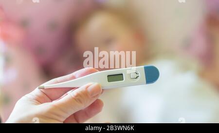 Nahmedizinisches Thermometer, Eltern messen die Temperatur des kranken Kindes, 1 Jahre altes Kleinkind, das hohes Fieber im Bett liegt. Fieber im Kind Stockfoto