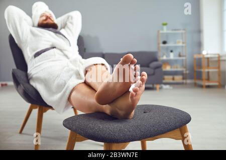 Lustiges Pediküre-Konzept. Lustiger fetter Mann im bademantel und ein Handtuch malt seine Nägel Stockfoto