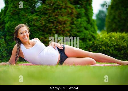 Selbstbewusste Schwangere Frau, Die Während Des Trainings Im Park Auf Der Seite Liegt Stockfoto