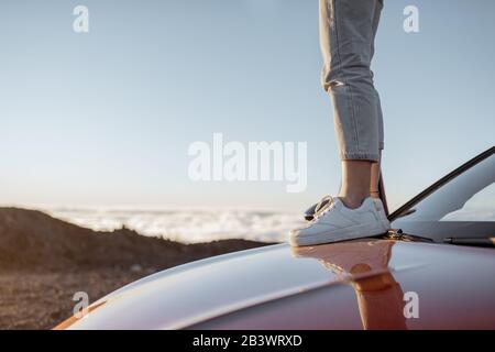 Frau, die auf der Autokombe steht, während sie über den Wolken unterwegs ist, Nahaufnahme von weißen Turnschuhen der Frau Stockfoto