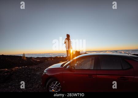 Junge Frau felsige Landschaften über den Wolken, die hoch in den Bergen auf dem Auto stehen. Sorgloses Lifestyle- und Reisekonzept Stockfoto