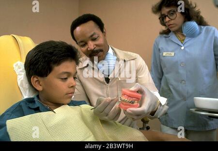 Austin Texas USA: Schwarzer Kieferorthopäde zeigt seinem jungen hispanischen Patienten anhand eines Zahnmodells mit Zahnspangen, wie Kieferorthopädie funktioniert. ©Bob Daemmrich Stockfoto