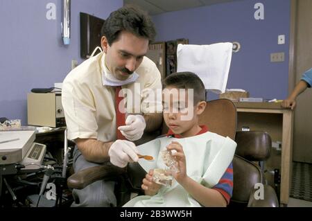 Austin Texas USA: Der hispanische Zahnarzt verwendet ein Zahnmodell, um jungen hispanischen Patienten den richtigen Weg zu zeigen, seine Zähne zu putzen. ©Bob Daemmrich Stockfoto