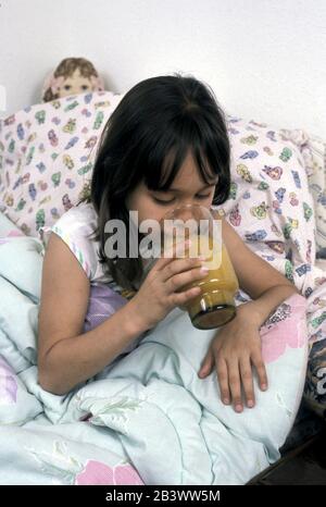 Austin, Texas USA: Ein siebenjähriges Mädchen, das an einer milden Erkältung leidet, trinkt ein Glas Orangensaft im Bett, bevor es einschläft. ©Bob Daemmrich Stockfoto