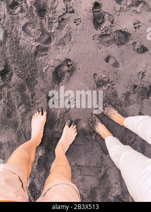Ein Paar steht am schwarzen Sandstrand. Nahansicht der Beine von oben. Bild auf Handy gemacht Stockfoto