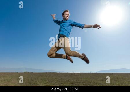 Wunderschöner, legerer Mann mit blauem Hemd, das im Freien hoch zum blauen Himmel springt Stockfoto