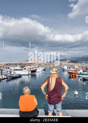 Spanien, TENERA, LAS GALLETAS, - 06. JANUAR 2020: Älteres Paar, das mit Jachten und Booten auf den Hafen in Las Galletas Dorf im Süden der Insel Tena blickt. Ansicht von der Rückseite Stockfoto