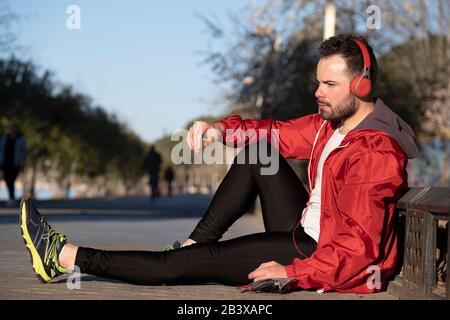 Junger Mann in Sportswear, der mit einem Paar Kopfhörern Musik hört Stockfoto