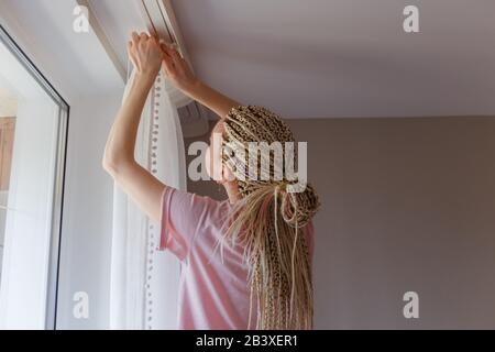 Frau hängte Gardinen am Fenster auf Stockfoto