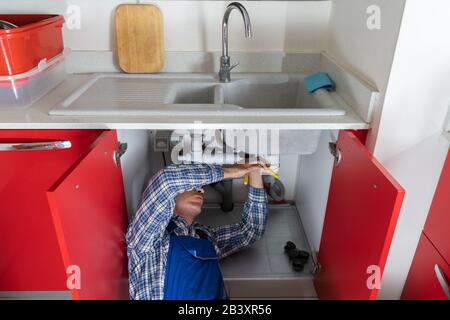 Junge Klempner Arbeiten mit Rohrzange In Küche Stockfoto
