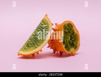 Ein orangefarbener Kiwano und ein halber Kinavo auf pinkfarbenem Hintergrund. Stockfoto