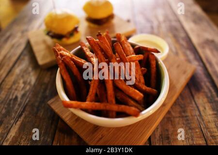 Titel: Gebratene Pommes Frites aus Süßkartoffel in der Schüssel auf rustikaler Holz-Tischplatte Stockfoto