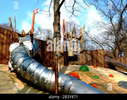 Edelstahlschlitten. Öffentlicher Park. Farbenfroher orangefarbener, gelber und grüner Gummi-Sicherheitsboden. Fröhliche Halbkugelformen und Muster. Baumhaus Stockfoto