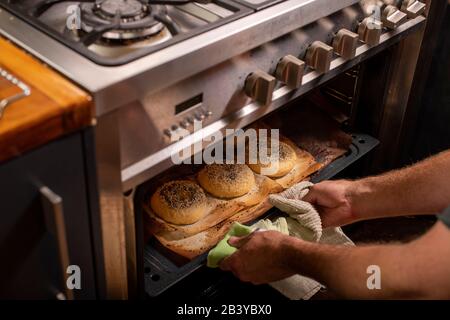 Koch greift mit zwei Händen, um frisch gebackene Bagels aus einem heißen Ofen zu ziehen Stockfoto