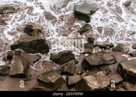 Wellen brechen, Meerwasser mit weißem Schaum, zwischen den Felsen des Ufers. Draufsicht. Stockfoto