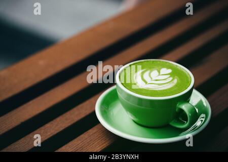 Matchbecher mit Latte Art auf Holzhintergrund. Schöner Schaum, grüner Keramikbecher, diagonale Komposition, Platz für Text. Stockfoto