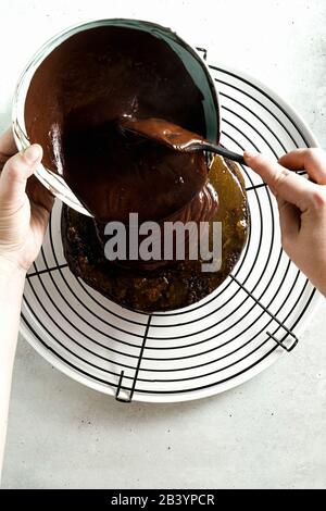 Schokoladenganache auf den Kuchen gießen, weibliche Hände Stockfoto