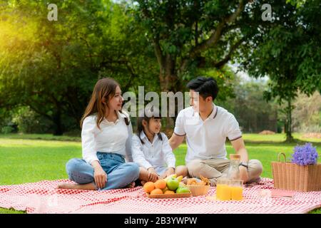 Asiatische Teenager Familie fröhlicher Urlaub Picknick-Moment im Park mit Mutter und Tochter, die Vater anschaut und lächelt, um glücklich zu verbringen Urlaub Zeit togerter ich Stockfoto