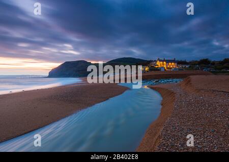 Seatown, Dorset, Großbritannien. März 2020. Wetter in Großbritannien. Blick auf den Strand in Seatown in Dorset kurz nach Sonnenuntergang nach einem Tag starken Regens mit dem Fluss Winniford, der über den Strand fließt, und in der Ferne befindet sich die markante Klippe von Golden Cap, die die höchste Klippe an der Südküste Englands ist. Neben dem Strand befindet sich das Anchor Inn. Bildnachweis: Graham Hunt/Alamy Live News Stockfoto