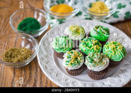 Ein Teller mit grünen und weißen Schokoriegeln aus Milchschokolade, die mit Gold-, Gelb- und Grün-Gesprengkuchen verziert sind. Verwischt im Backg streuen Stockfoto