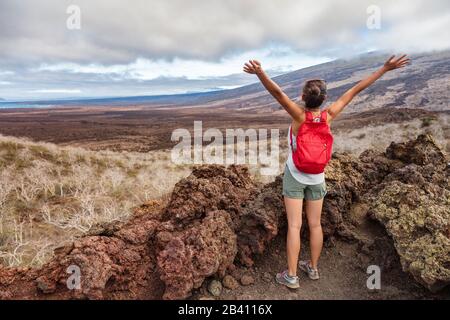 Galapagos Touristenwanderungen auf der Insel Santiago, den Galapagos-Inseln, Ecuador, Südamerika. Frau auf der Wanderung, die Sehenswürdigkeiten und Touristenattraktionen besucht. Glücklich und aufgeregt, wenn die Arme in den Himmel erhoben werden. Stockfoto