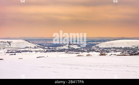 Schneebedeckte Felder der Purbeck Hills umgeben das Schloss Corfe unter stürmischem Himmel Stockfoto