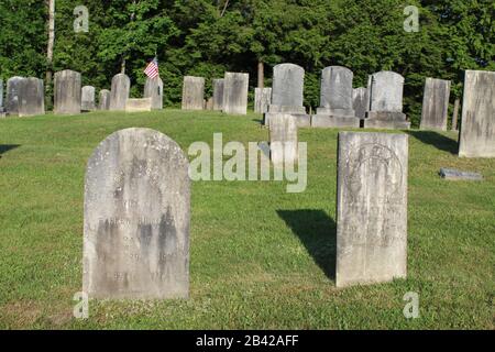 Hohe graue Kopfsteine auf einem kleinen Friedhof in Vermont mit US-Flagge im Hintergrund Stockfoto