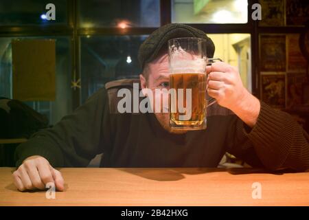 Der rothaarige, fast irischstämmige Kerl sitzt in der Bar und trinkt etwas Bier und schaut mit lustigem Gesicht auf Sie Stockfoto