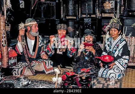 Ein bärtiger Ainu-Mann und drei Frauen posieren im traditionellen Kleid mit Ainu-Souvenirs, die sie in einem einheimischen Haus verkaufen, das Touristen auf der Insel Hokkaido im Norden Japans offen steht. Dahinter stehen Lackkassen, die Familienschätze aufnehmen. Die älteste Frau im Alter von 84 Jahren hat ein Tattoo um den Mund, das einem Schnurrbart ähnelt. Die schmerzhafte Tradition, während der Kindheit von Ainu-Mädchen Ruß in Hautschnitte zu reiben, um böse Geister abzuwehren, wurde seitdem von der japanischen Regierung geächtet. Das waren 4 von nur 300 reinblütigen Ainu, die noch lebten, als diese historische Fotografie 1962 aufgenommen wurde Stockfoto