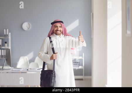 Ein glücklicher arabischer Mann hob seinen Daumen in einem weißen Büro auf Stockfoto
