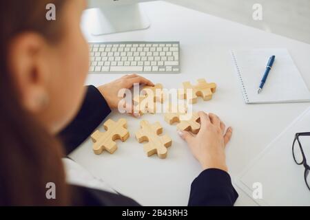 Gesichtslose Hände einer Geschäftsfrau mit Holzrätseln auf einem weißen Tisch im Büro. Stockfoto