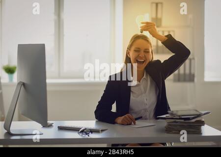 Eine Frau in einem Business-Anzug hält eine leuchtende Lampe in den Händen an einem Tisch im Büro. Stockfoto