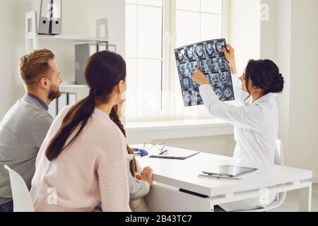 Eine Familie, die einen Arzt besucht, zeigt Röntgenaufnahmen, die an einem Tisch im Zimmer sitzen. Stockfoto