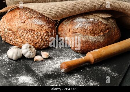 Hausgemachtes traditionelles Brot, auf einem Tisch mit Mehl bestreut, bedeckt mit einem Stück Burlap, neben Knoblauch und einem Rollstift. Stockfoto