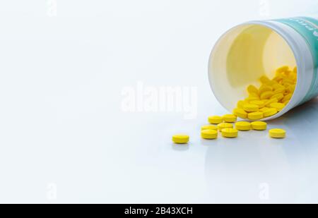 Gelbe Tablettenpillen verteilen sich aus der Medikamentenflasche. Tabletts Tabletten mit Flasche auf weißem Tisch. Medikamentenproduktion im Konzept der pharmazeutischen Industrie. Gesundheit Stockfoto