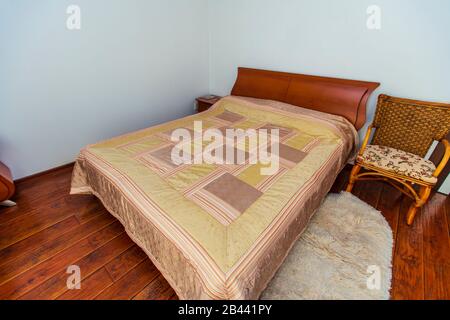 Ein großes Schlafzimmer mit Mahagoni, Korbstühlen und einem eleganten Schminktisch mit einem halbkreisförmigen Spiegel. Das Bett hat eine beige Decke in Quadraten. Stockfoto