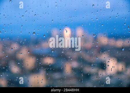 Regentropfen auf einer Glasscheibe mit verschwommenem Hintergrund der Themse und des Finanzviertels der City of London Canary Wharf Stockfoto