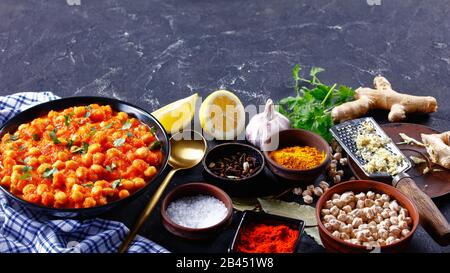 Gesundes indisches Chana Masala oder Kichererbsencurry mit Zutaten auf dunklem Betongrund: Kurkuma, Chili, Ingwer, Knoblauch, Nelken, Lorbeerblatt, Zitrone Stockfoto