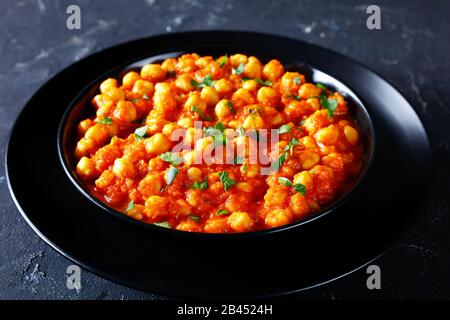 Indischer Festtagskurs Chana Masala oder Kichererbsencurry mit Gewürzen, Tomatensauce, Zwiebel, Knoblauch, rotem Chilipuder, mit Petersilie auf Schwarz bestreut Stockfoto