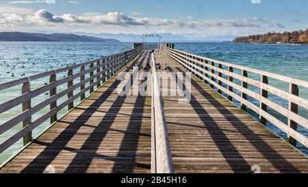 Gerader Blick auf einen Holzsteg am Starnberger See (Starnberger See). Alpen in der Ferne. Konzept für Chance, Neubeginn, Chancen, Start. Stockfoto