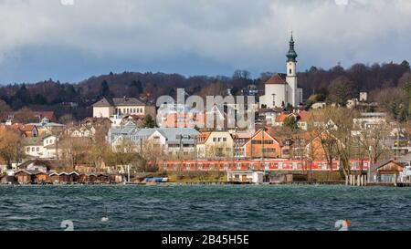 Blick auf die Stadt Starnberg. Mit der Kirche St. Josef (Sankt Josef), einem roten S-Bahn-Zug & Bootshaus. Im Vordergrund der Starnberger See. Stockfoto