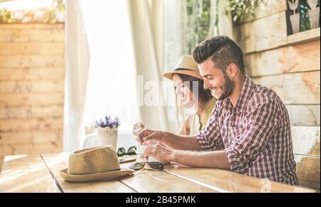 Fröhliches junges Paar, das Kaffee trinkt und in der Café-Bar verwendet - Trendige Touristen, die im Urlaub frühstücken - Reisen, Liebe, Essen und Beziehung Stockfoto