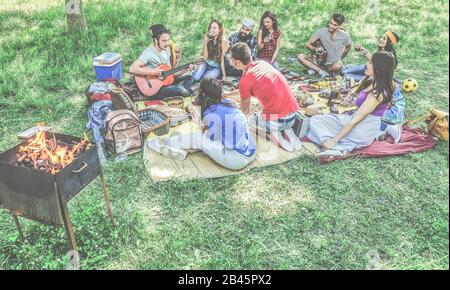 Eine Gruppe von Freunden, die im Stadtpark einen Picknickgrill machen - Junge Leute, die Spaß beim Musikspielen haben und sich auf der grillparty auf Gras entspannen - Main