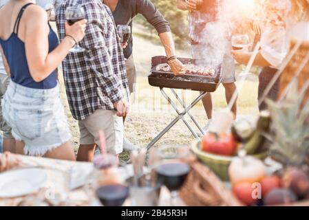 Eine Gruppe von Leuten, die im Freien Picknickgrill in der Natur haben - Fröhliche Freunde, die am Wochenendsommertag Fleisch kochen und Wein trinken - Familie, Essen und Stockfoto