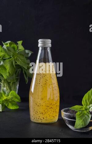 Tropischer Orangensaft mit Basilikumsamen in der Flasche auf schwarzem Hintergrund. Nahaufnahme. Vertikales Format. Stockfoto