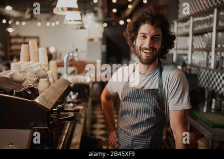 Portrait des hübschen jungen männlichen Kaffeehänders, der hinter der Theke steht Stockfoto