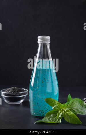 Blauer Cocktail aus verschiedenen tropischen Früchten mit Basilikumsamen in Flasche auf schwarzem Hintergrund. Nahaufnahme. Vertikales Format. Entgiftung und Frische. Stockfoto
