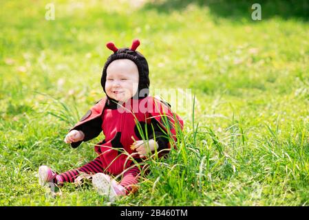 Süßes und fröhliches Porträt des kleinen Kindes, das in blühenden Blumen von Löwenzahn in Marienkostüm sitzt. Vorstellung von Halloween Kindheit und Stockfoto